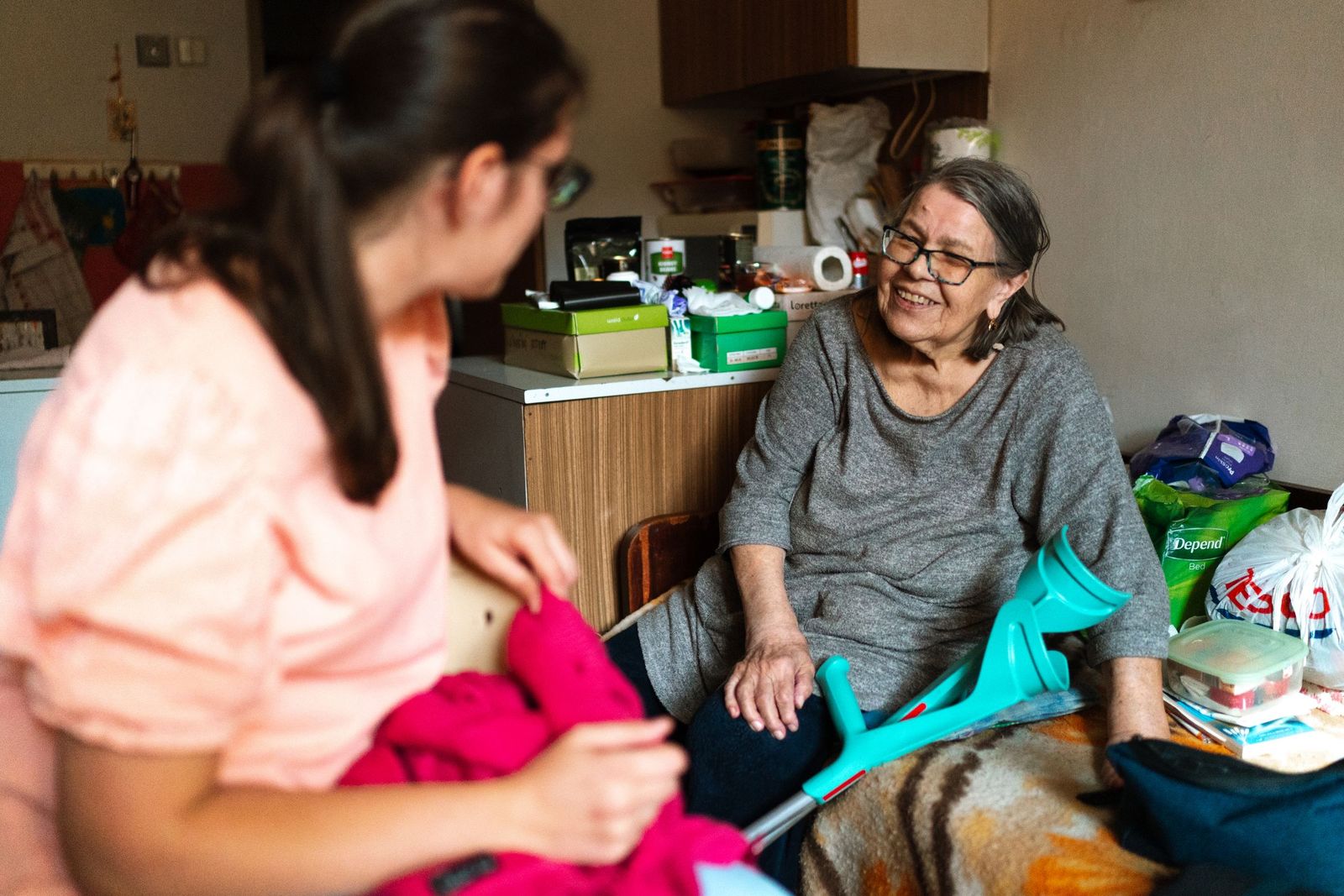 Caregiver sitting with an older woman who uses crutches at home